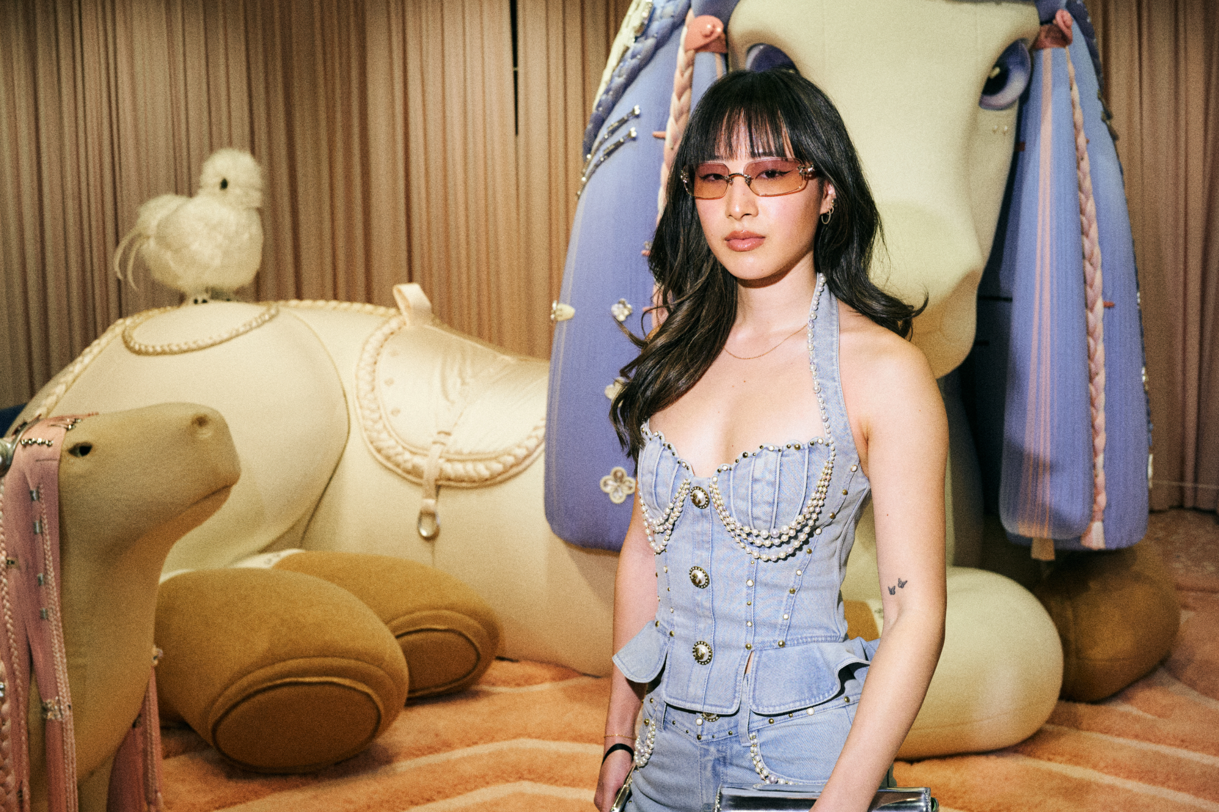 Woman in denim bustier outfit with decorative chains, posing with whimsical animal sculptures
