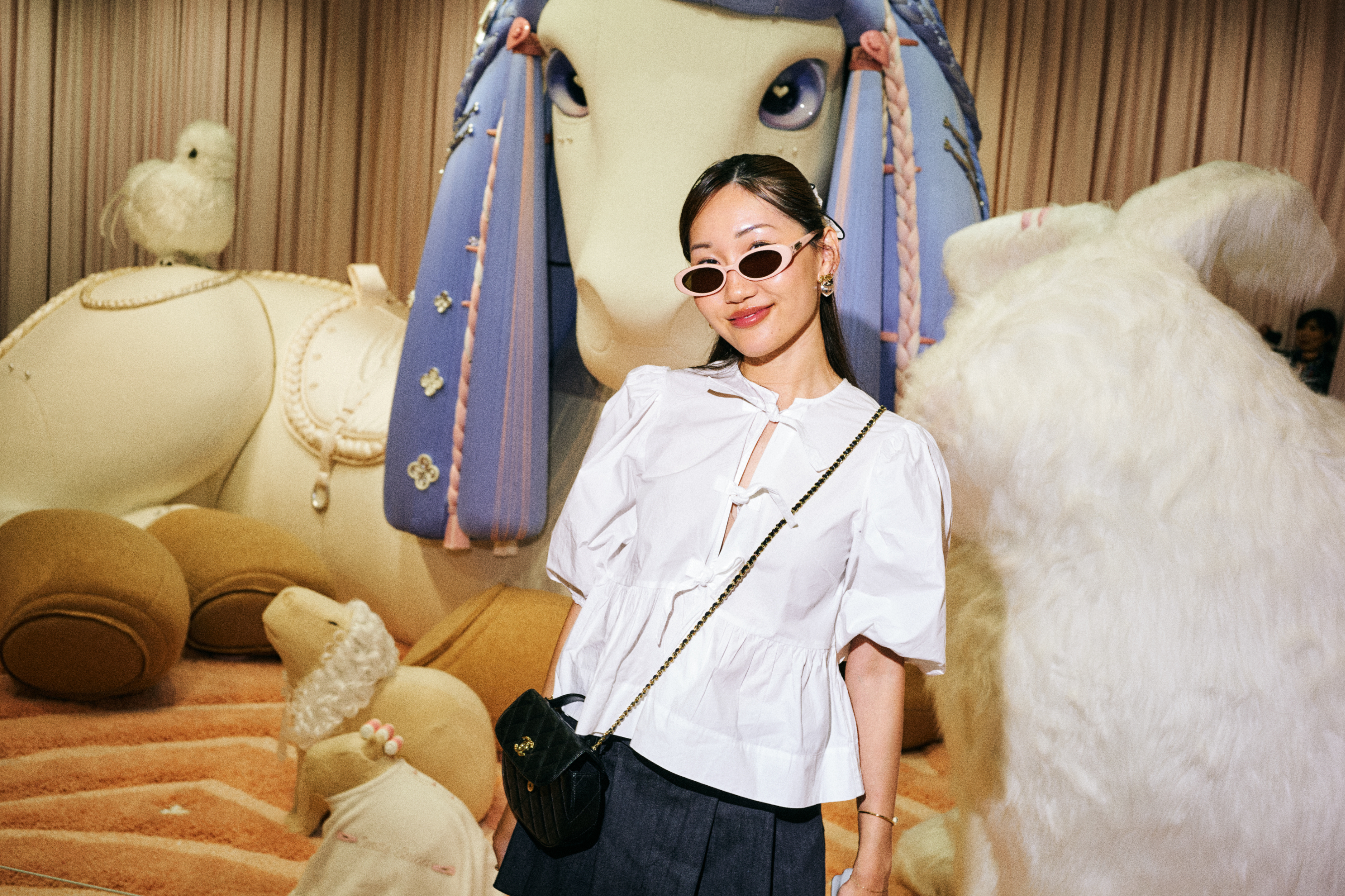 Woman poses in a ruffled white blouse and dark skirt, with plush toys in the background