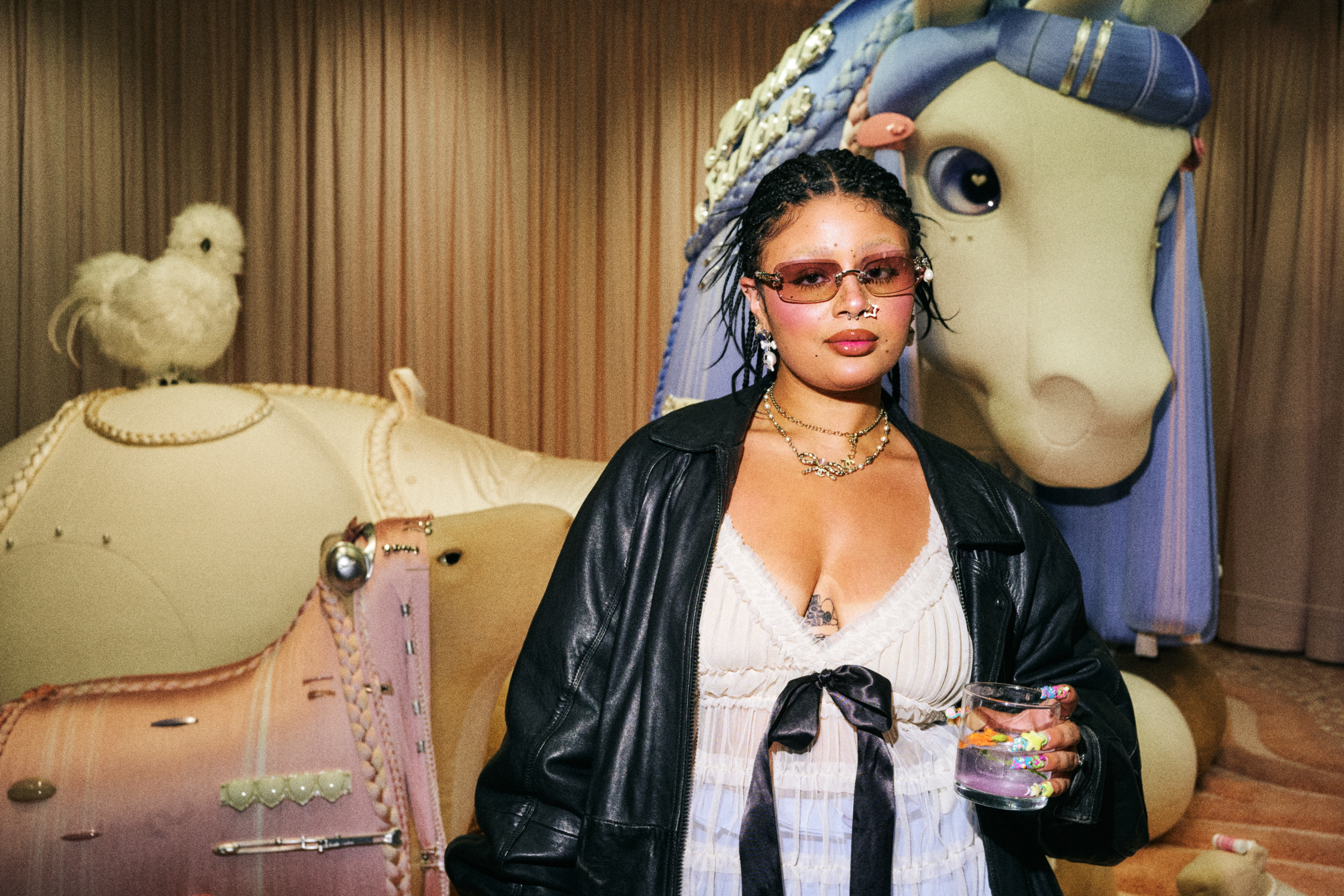 Woman in white corset top and black jacket at event, standing near large toy horse