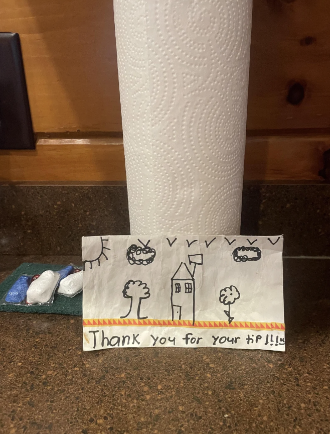 Hand-drawn thank you sign with illustrations of a house, sun, and cars, placed in front of a paper towel roll
