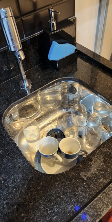 Kitchen sink filled with clear glasses and two white mugs waiting to be washed