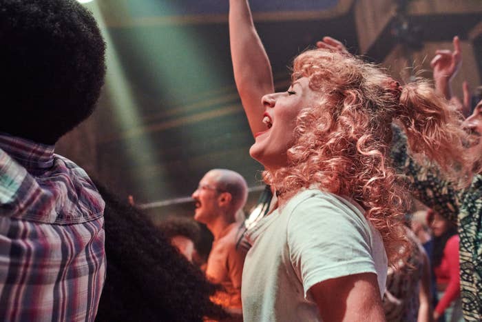 Woman with curly hair cheering at a concert, surrounded by other fans