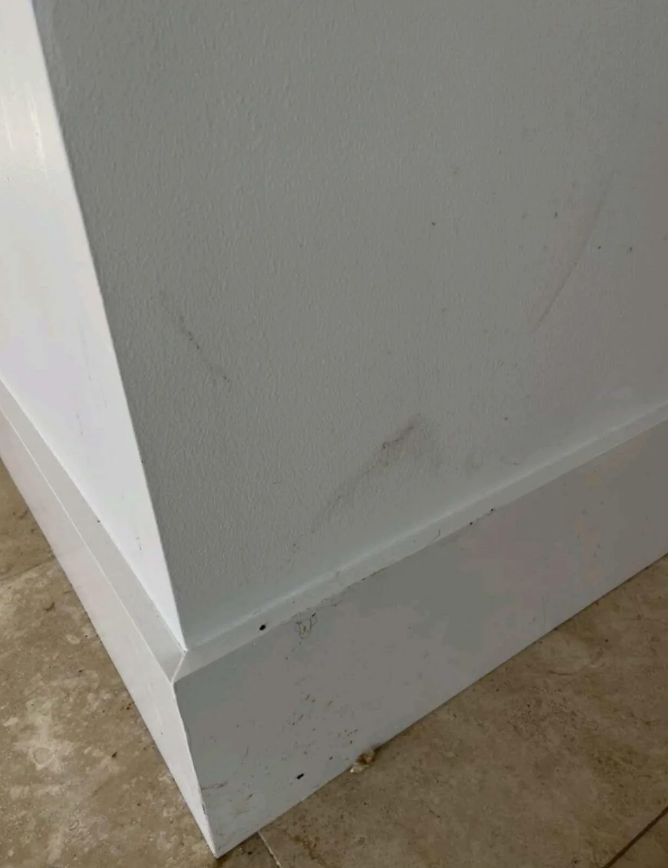 Corner of a white wall and baseboard with mild scuff marks