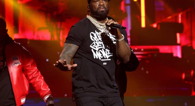 Rapper on stage performing, wearing a graphic tee, chain necklace, and cap
