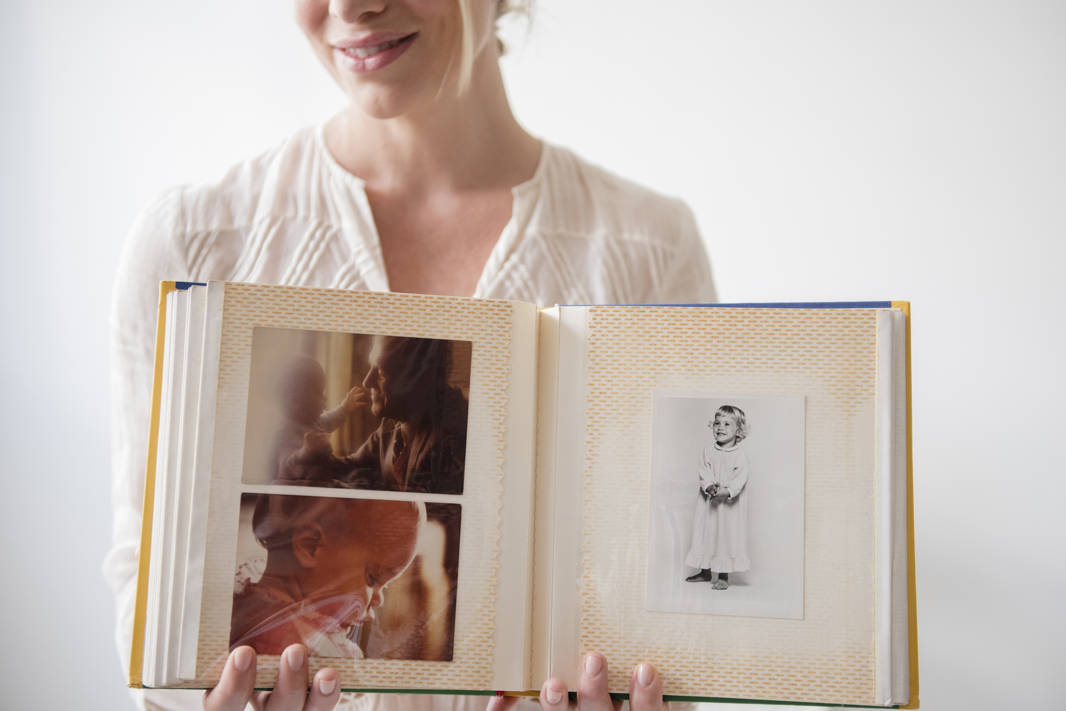 Woman smiling, holding open photo album with assorted family pictures
