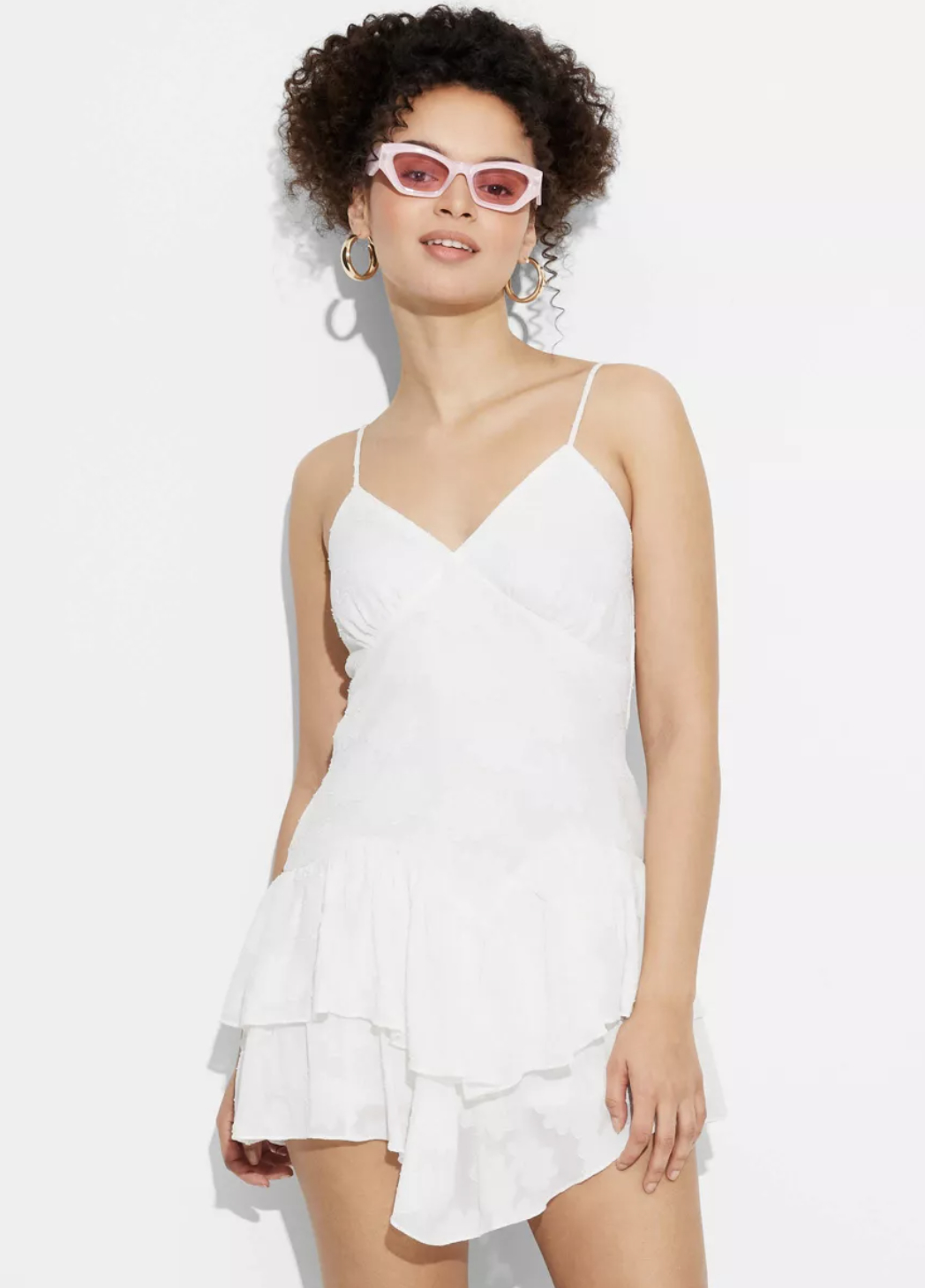 person in a white ruffled dress with sunglasses and hoop earrings