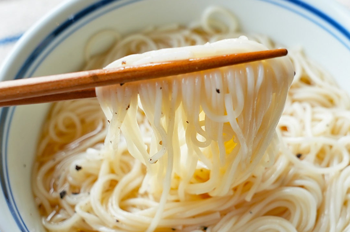 箸でつままれた白い麺が盛られたどんぶりです。