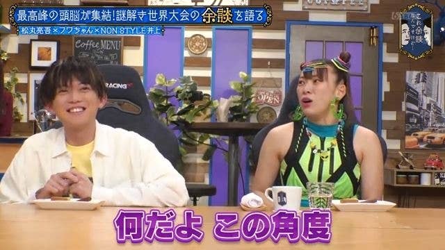 二人の男性がテーブルに座って話している。左は黄色い服を、右は緑色の明るい衣装を着ている。