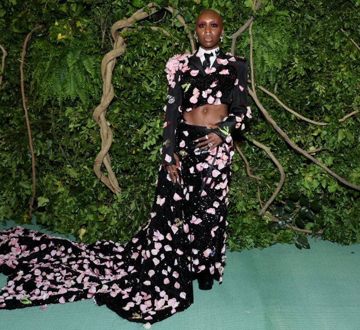 Person in a floral patterned dress with a long train, standing in front of a leafy backdrop
