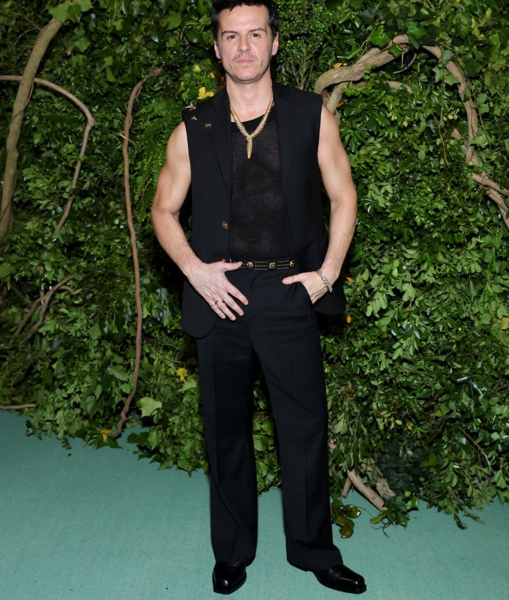 Man in a sleeveless top and black trousers posing with hand on hip