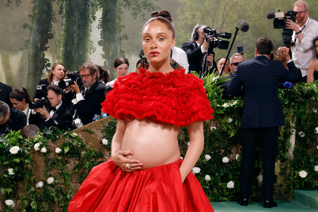 Pregnant woman in a red ruffled dress posing with hand on hip, photographers in background