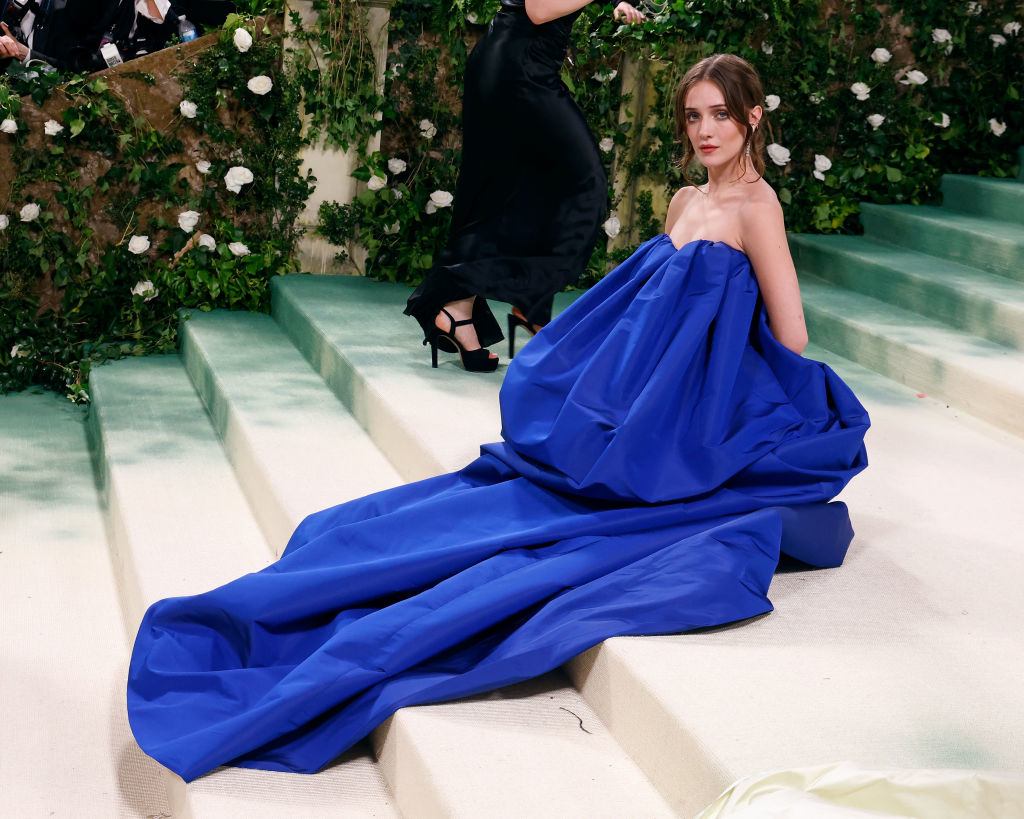 Talia in an elegant blue gown with a voluminous skirt sits on steps at an event