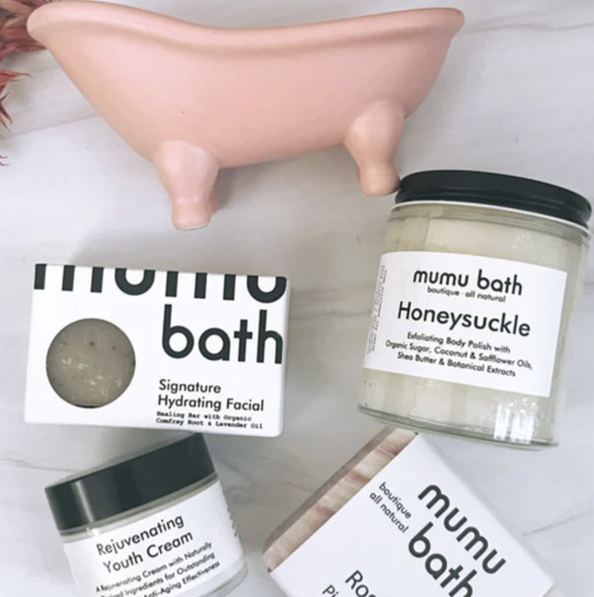 A selection of Mumu Bath skincare products including a soap, facial hydrator, and body polish