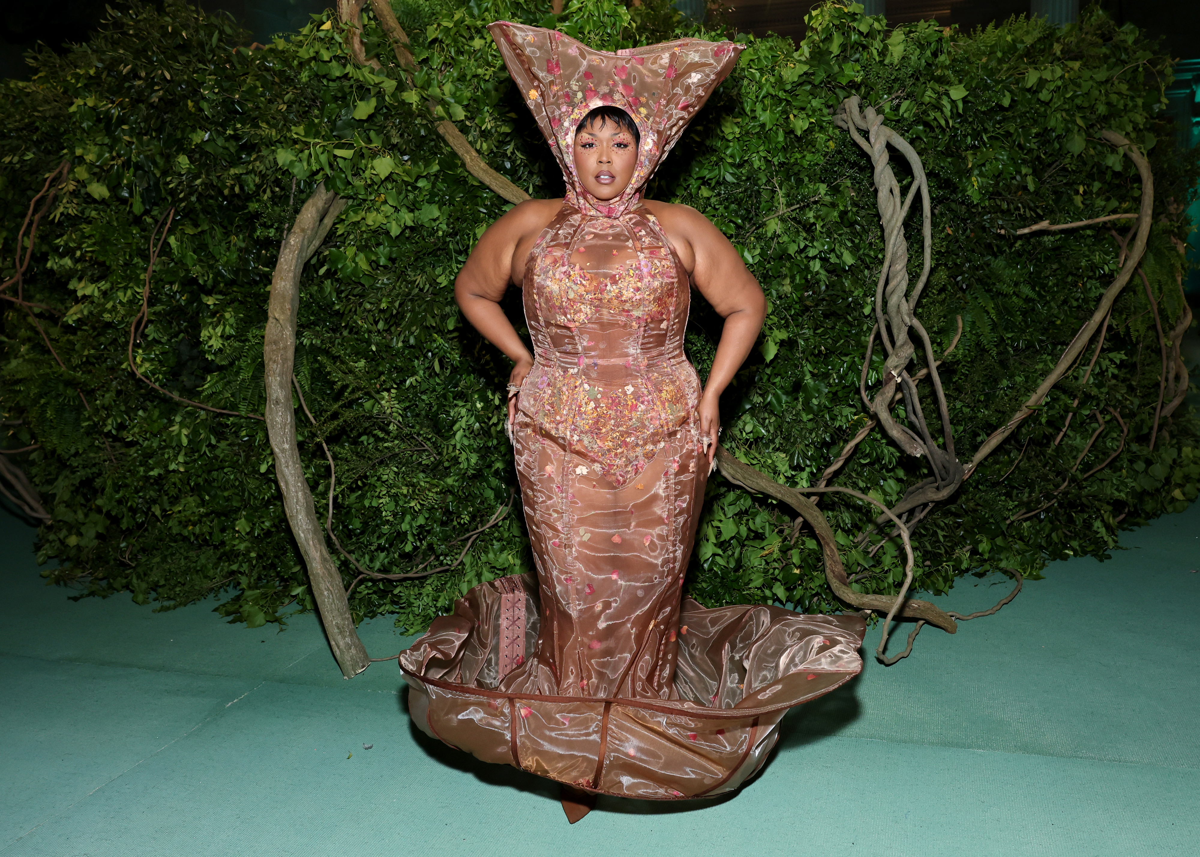 Lizzo wears a figure-hugging shimmering gown with an oversized headpiece at an event