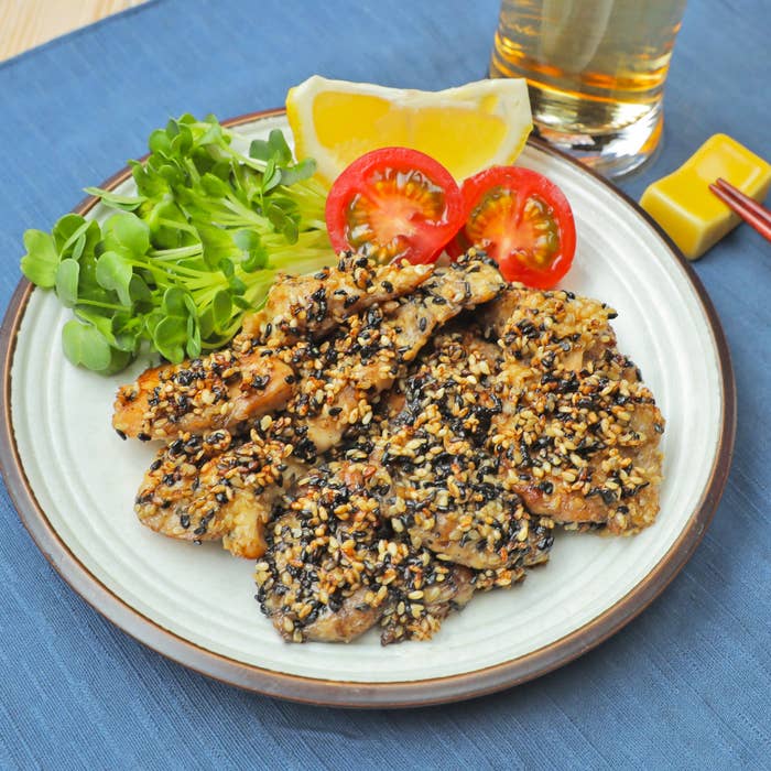 皿の上にごまをまぶしたチキンとレモン、トマト、サラダが添えられている。