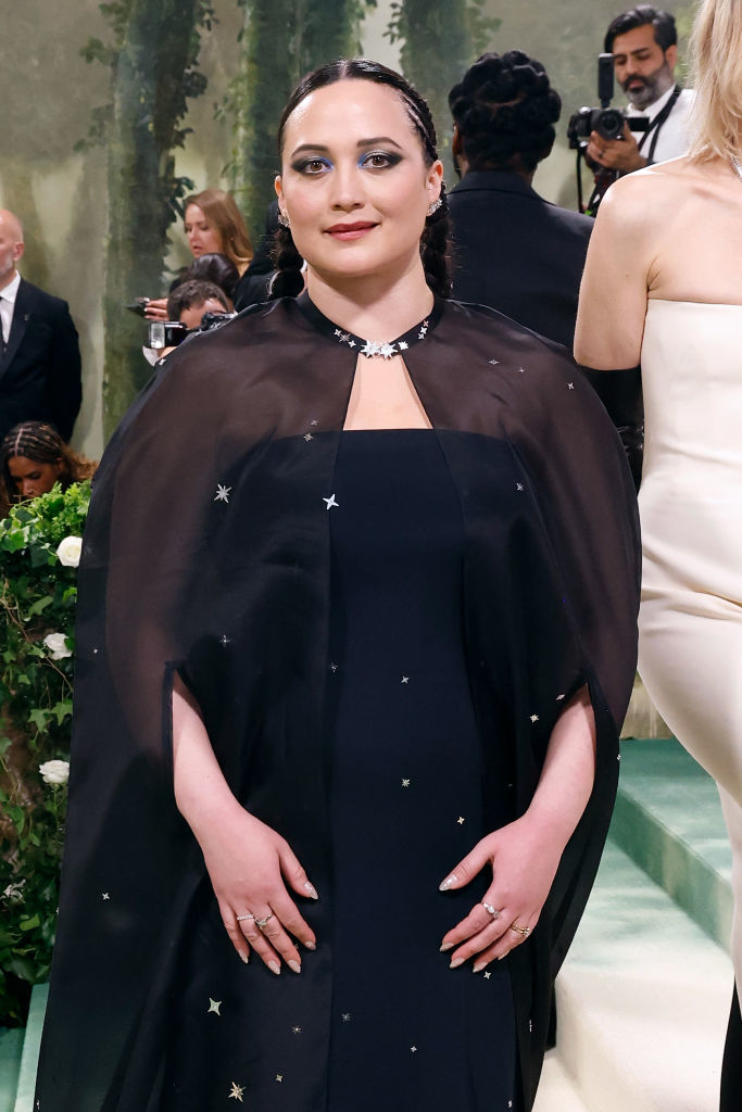 Lily Gladestone in a black outfit with star details and a cape, posing at an event