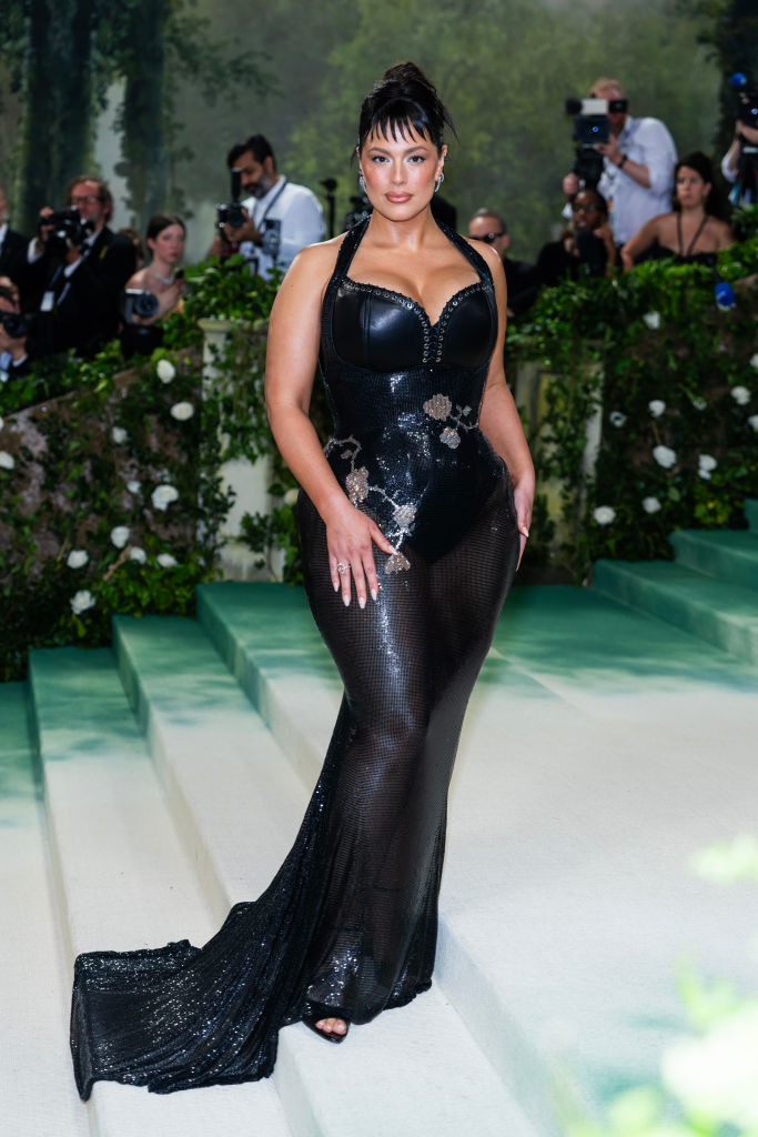 Ashley Graham in a black embellished gown with a mermaid silhouette on the red carpet. Photographers in the background