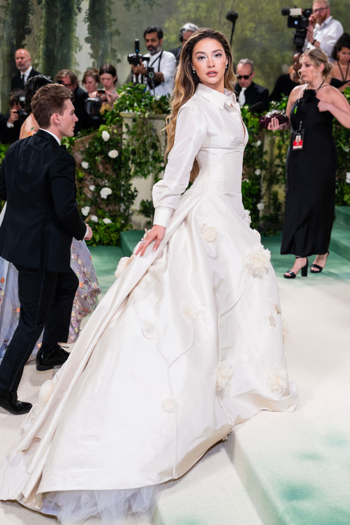 Madelyn Cline in elegant white gown with floral applique on a gala event backdrop