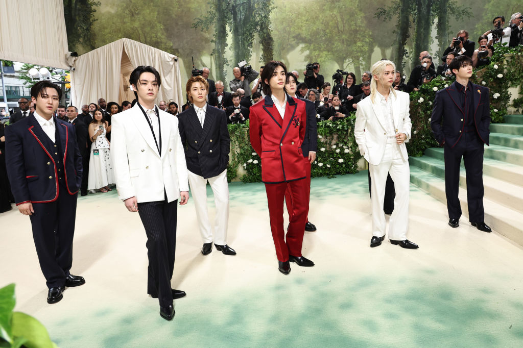 BTS members in an array of formal suits, the center member in a red suit, during an event