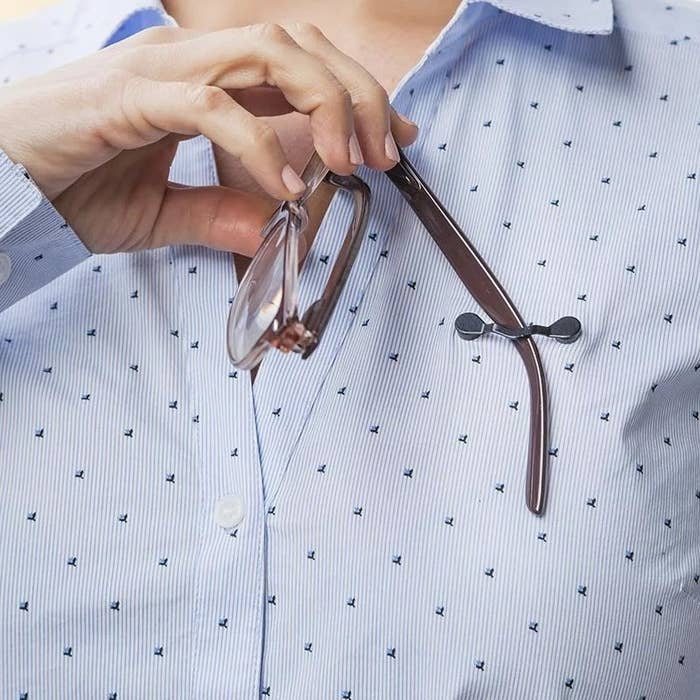 Orang yang mengaitkan salah satu kaki kacamata ke dudukannya, yang dipasang pada kemeja bergaris