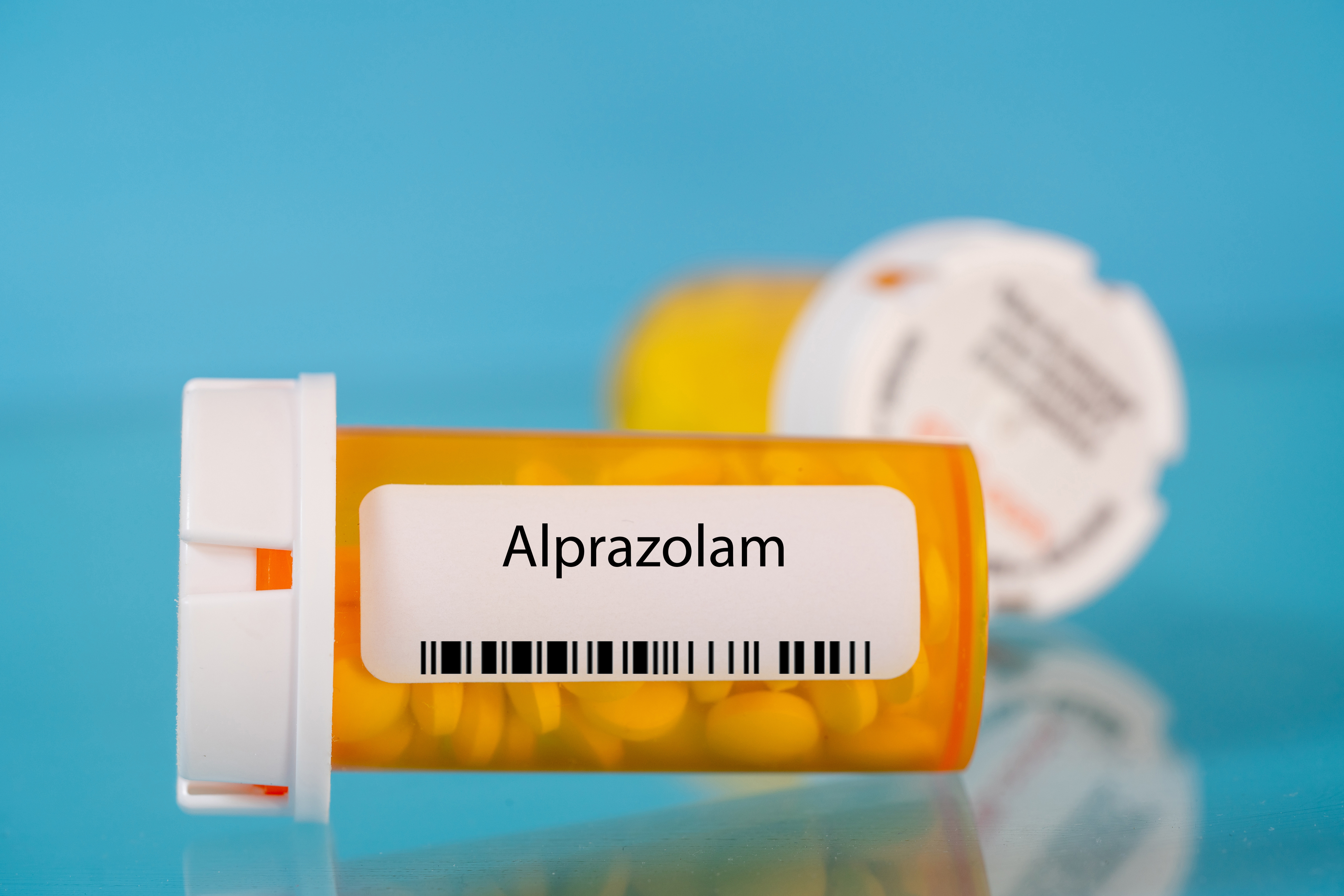 Prescription bottle labeled Alprazolam with pills, focused foreground on blue surface