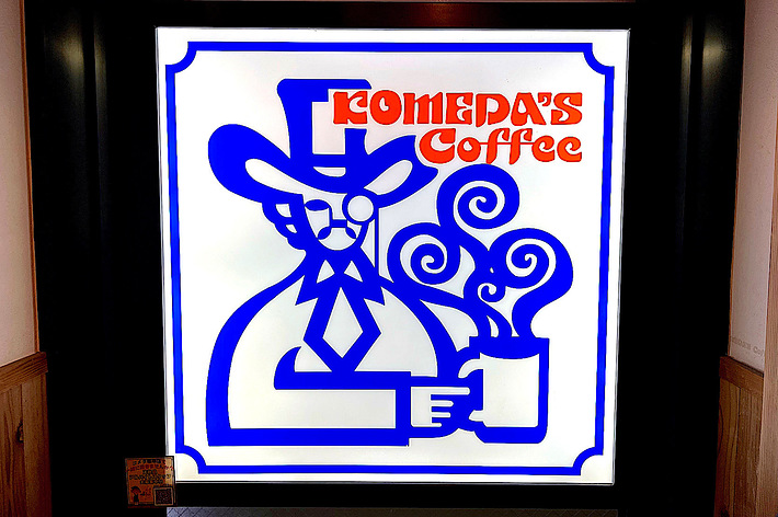 Sign for “TOMEDA’S Coffee” featuring stylized artwork of a person wearing a hat and holding a steaming cup