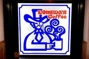 Sign for "TOMEDA'S Coffee" featuring stylized artwork of a person wearing a hat and holding a steaming cup