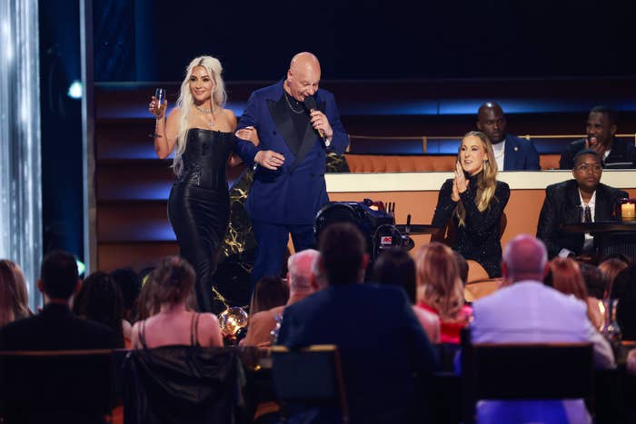 Lady Gaga in a black dress holding a microphone with a male presenter on stage at an awards ceremony