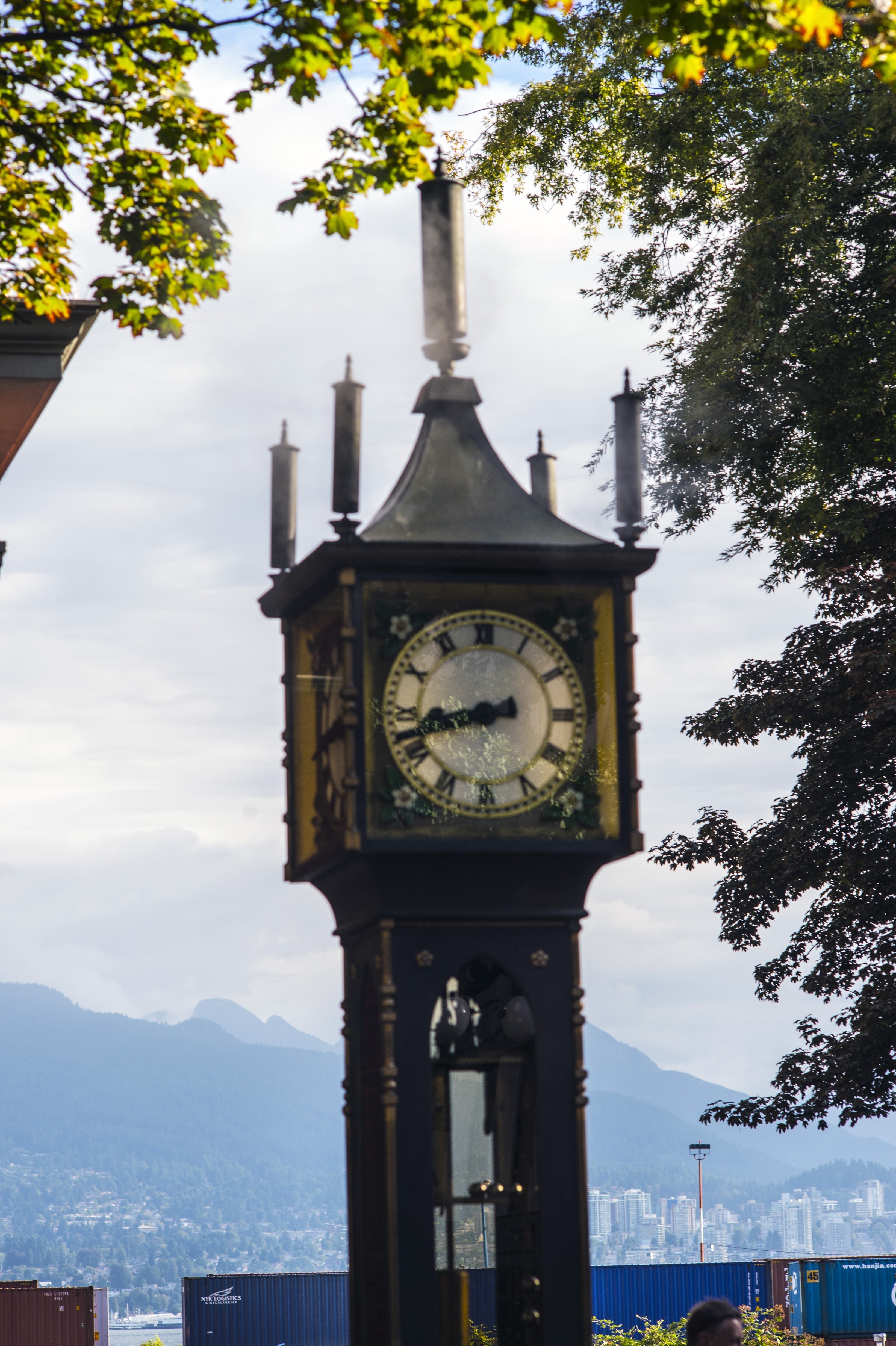 Historic steam clock in an urban setting with trees and a mountainous backdrop