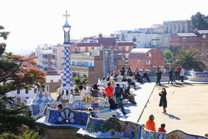 Visitors at Park Güell on a sunny day, with Gaudí's mosaic designs and unique architecture visible