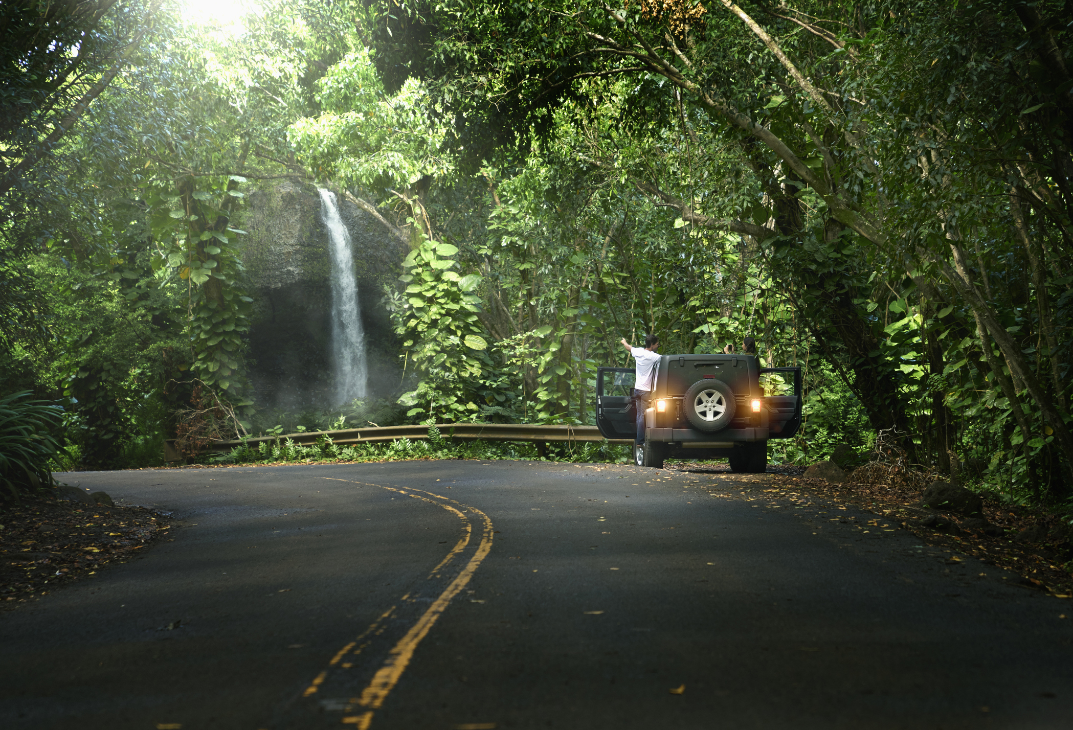 Car on forest road with a waterfall by its side