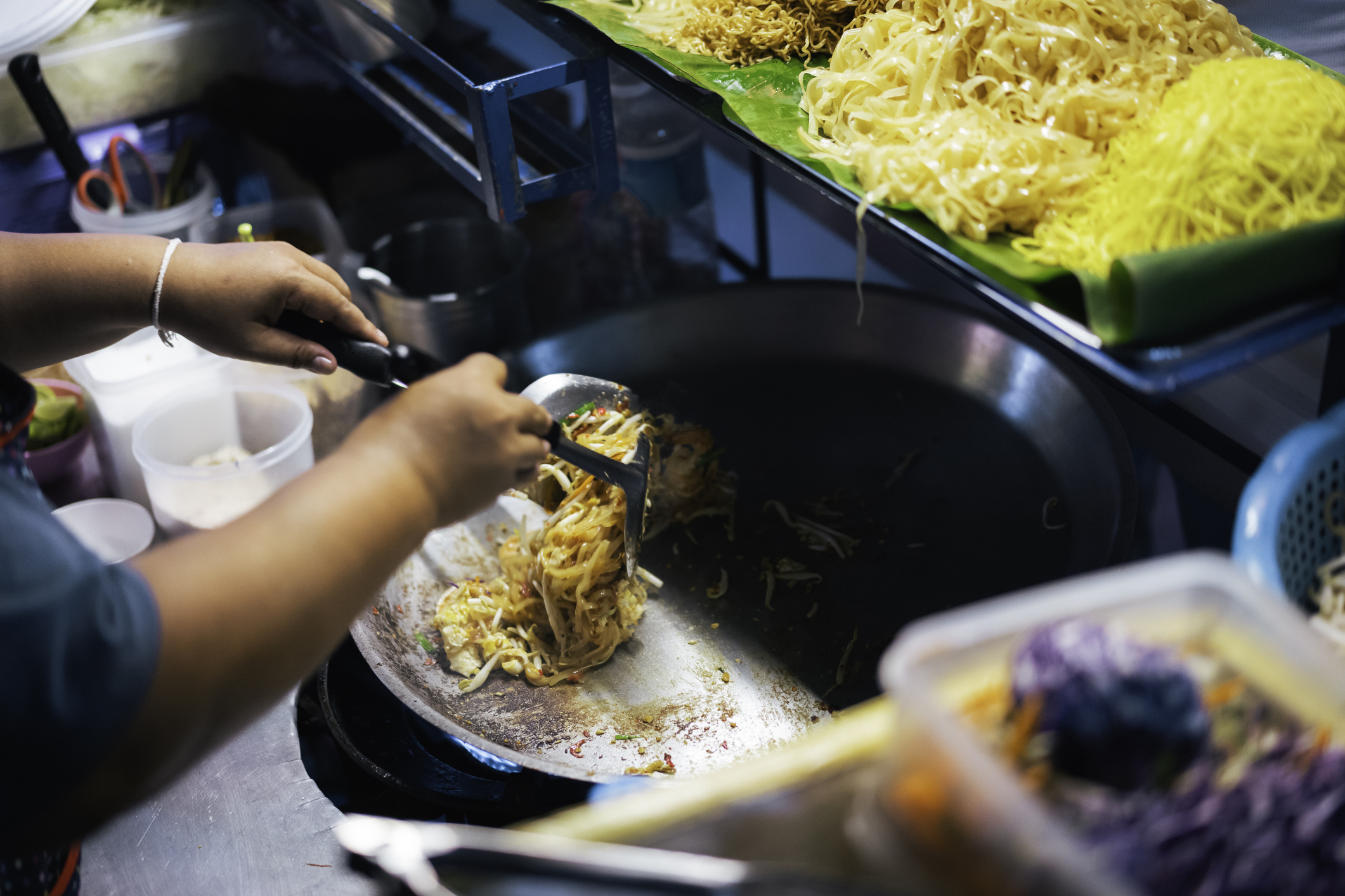 Person cooking noodles on a stove at a street market stall