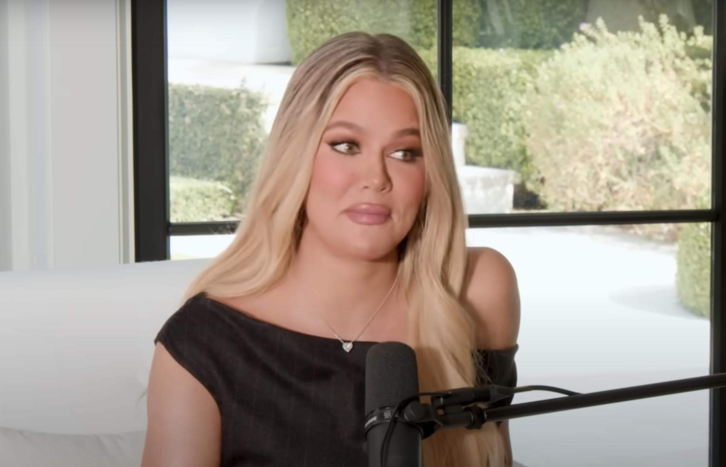 Khloe Kardashian in a black top with long blonde hair speaking into a microphone during an interview