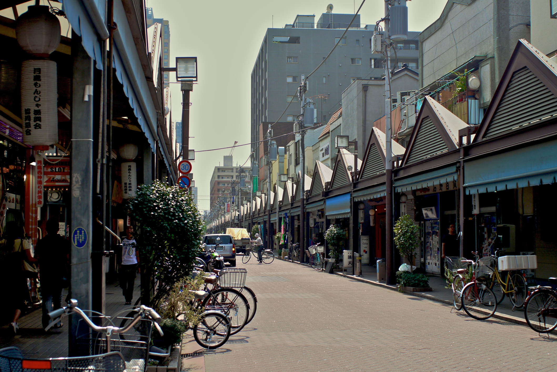 Street with bicycles and pedestrians, lined by single-story shops and a clear sky