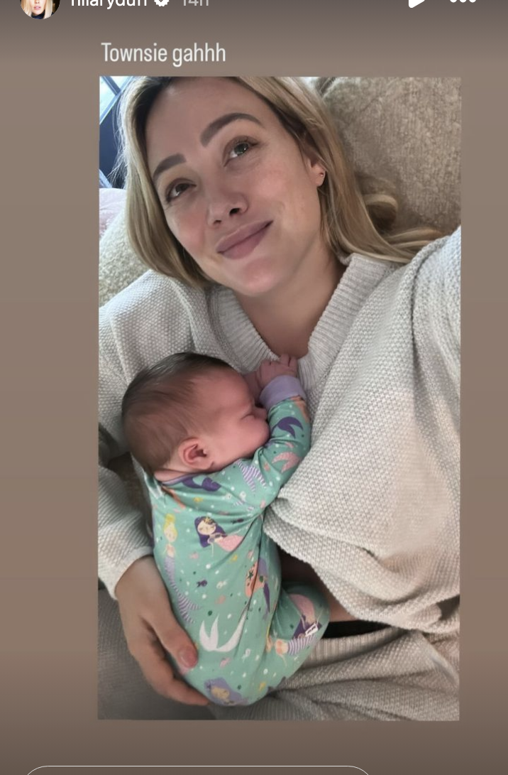 Hilary Duff takes a selfie while holding her sleeping newborn; both are in comfortable home clothing