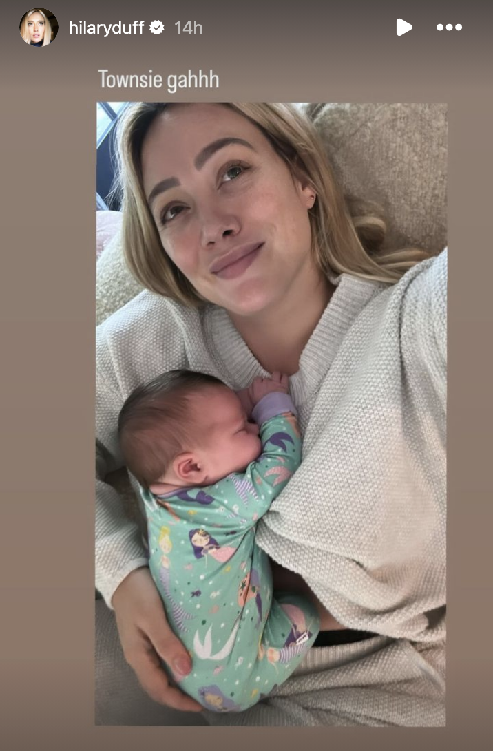 Hilary Duff takes a selfie while holding her sleeping newborn; both are in comfortable home clothing