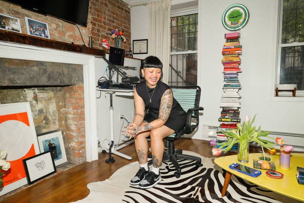 Person seated on an office chair, smiling, wearing sneakers in a room with eclectic decor