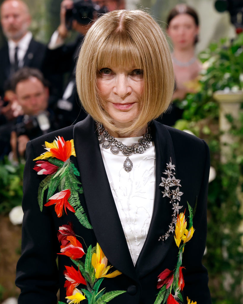 Anna Wintour in a black suit with vibrant floral embroidery, attending an event