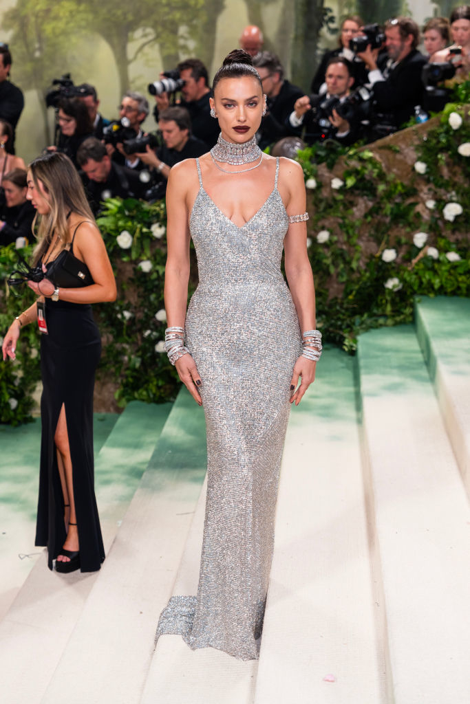 Irina Shayk on red carpet in glittery, sleeveless gown with choker neckline and matching bracelets
