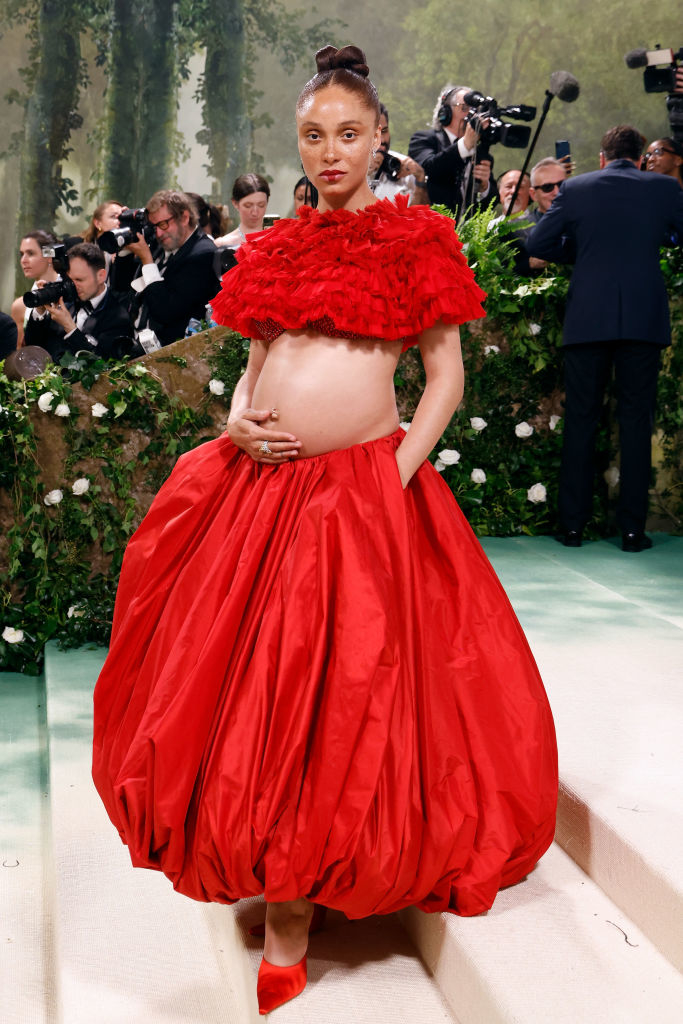 Rihanna in a ruffled red dress cradling baby bump on the red carpet