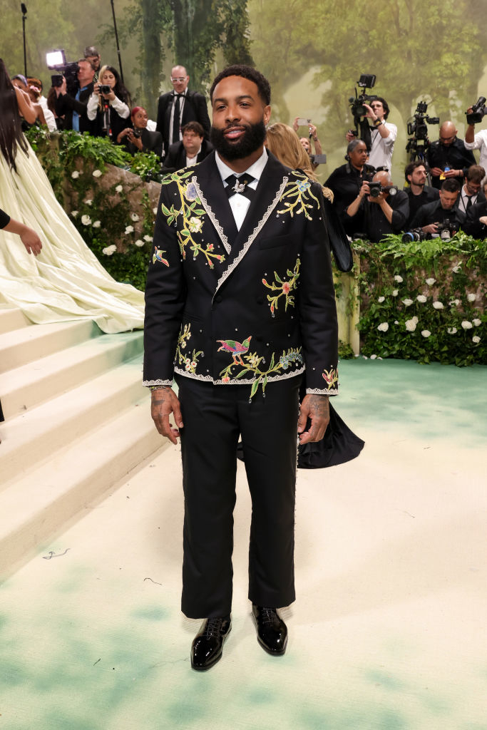 Odell Beckham Jr in embroidered suit on event stairs; photographers in background