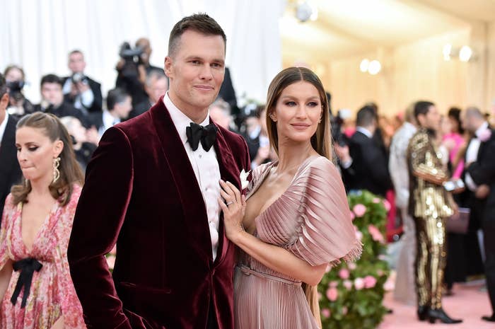 Tom Brady and Gisele Bundchen at an event, wearing a velvet suit and a pleated gown respectively