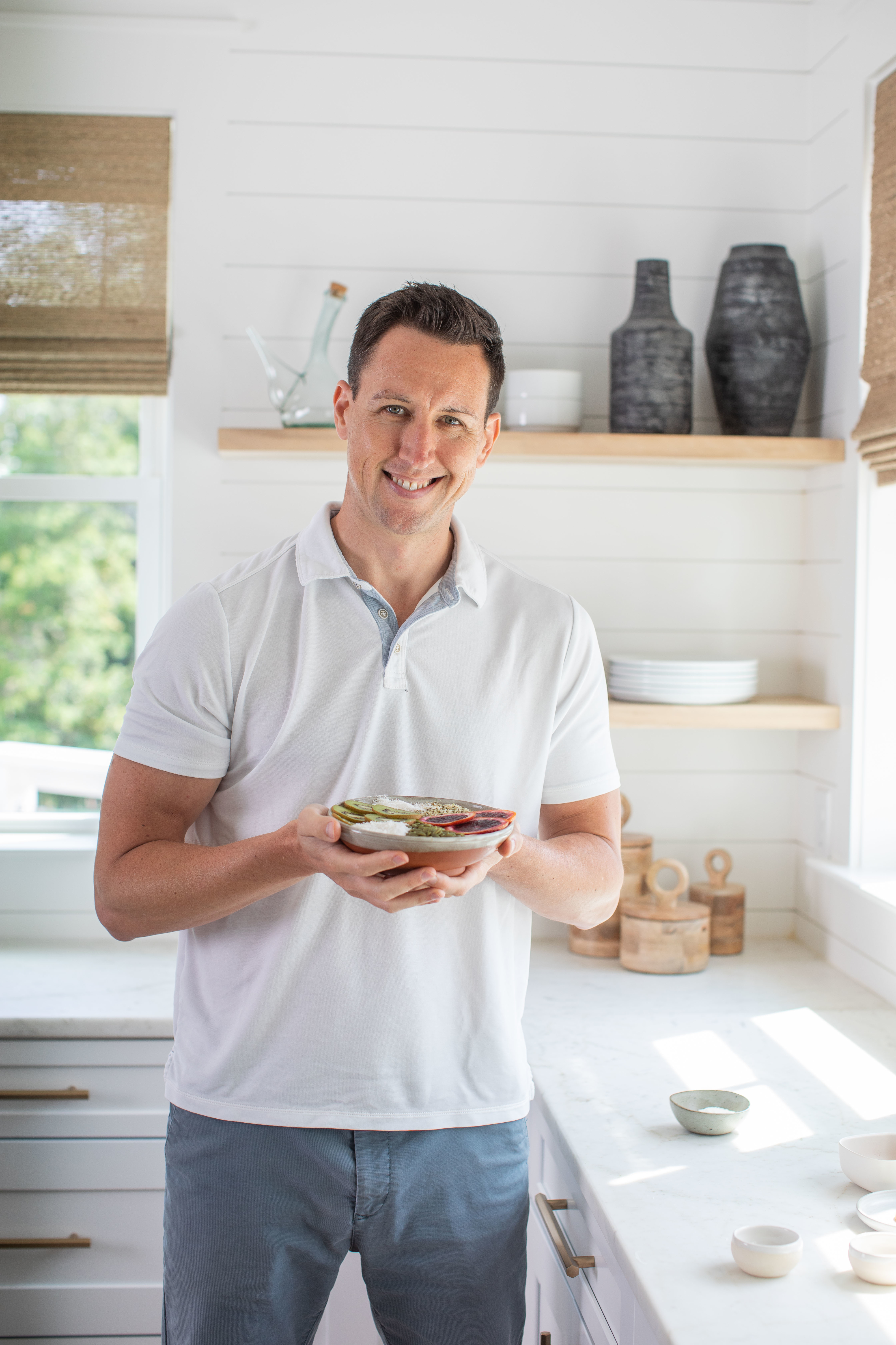Man holding a bowl of food in a kitchen, smiling at the camera