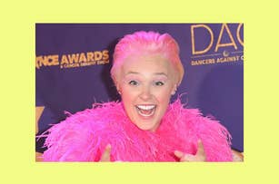 Individual with pink hair and feathery top gives a thumbs-up at the Dance Awards event