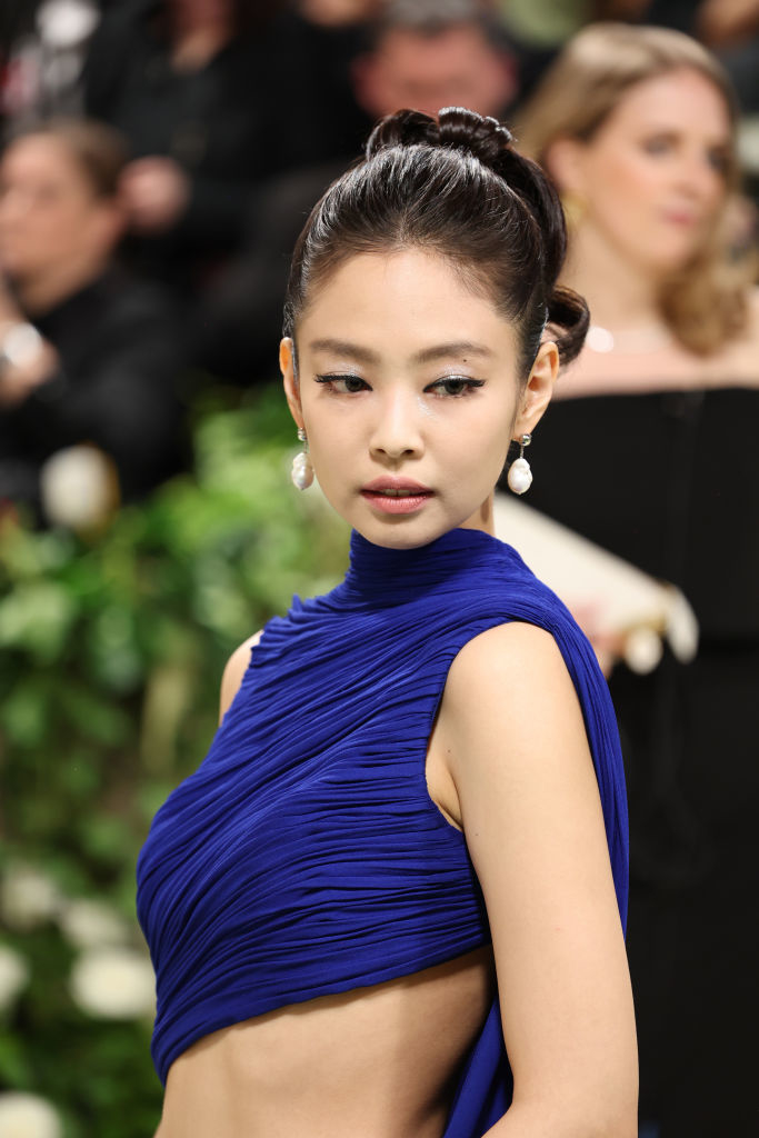 Jennie Kim in a blue high-neck gown with hair updo and earrings, looking over shoulder
