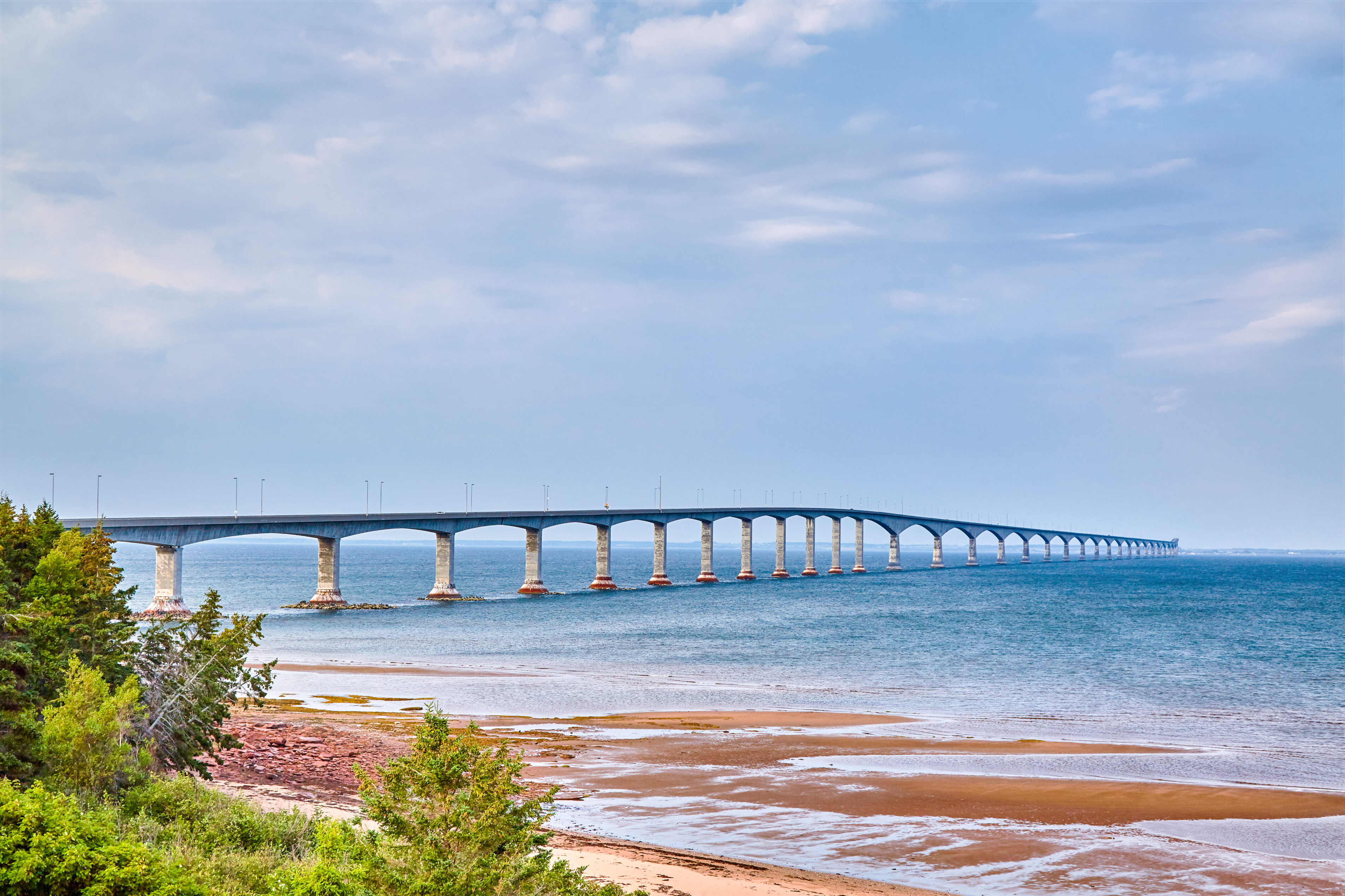 Long bridge extending over calm water with sandy beach in the foreground