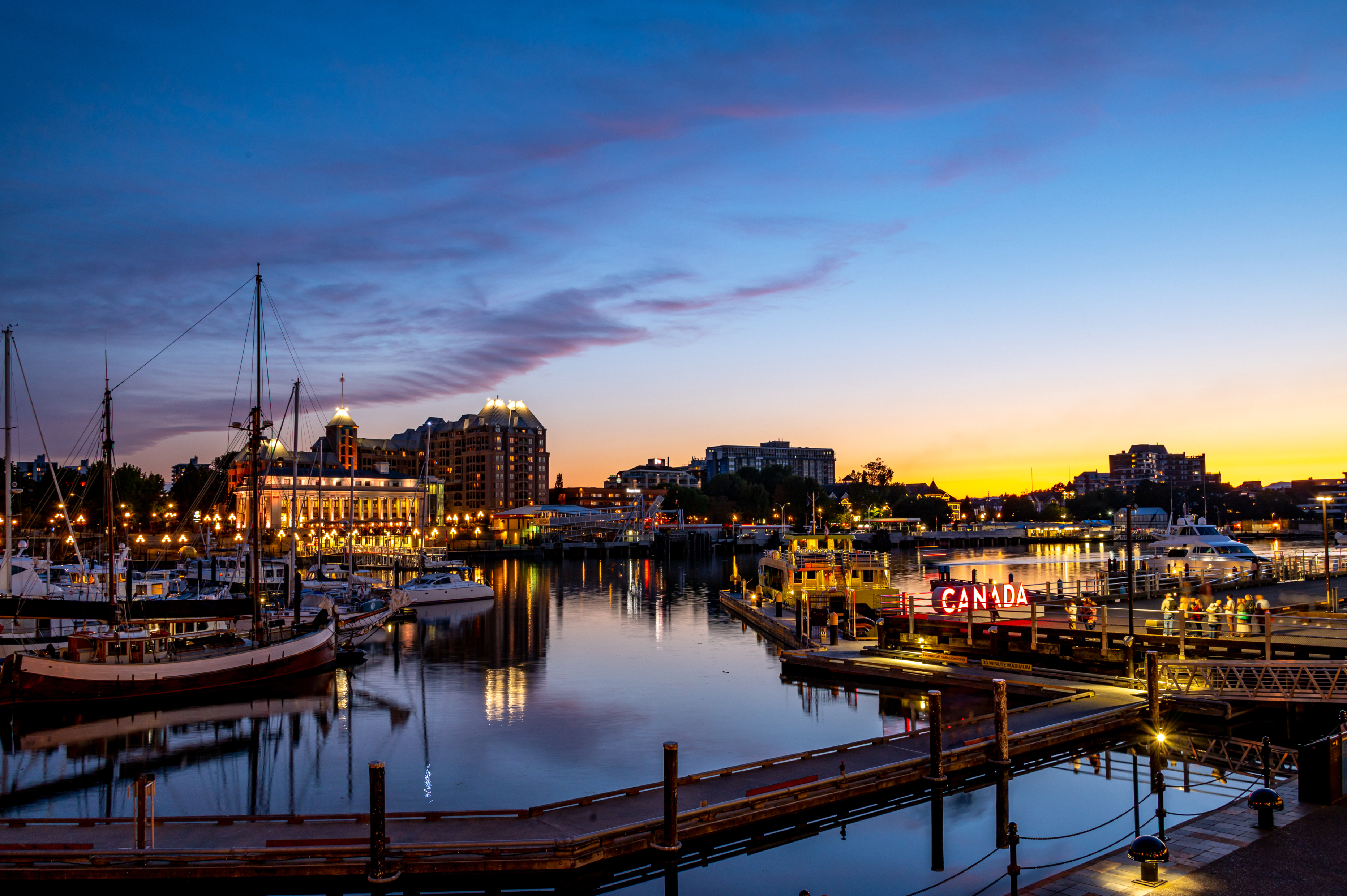 Harbor with boats at dusk, city skyline in the background, large &quot;CANADA&quot; sign illuminated on the dock