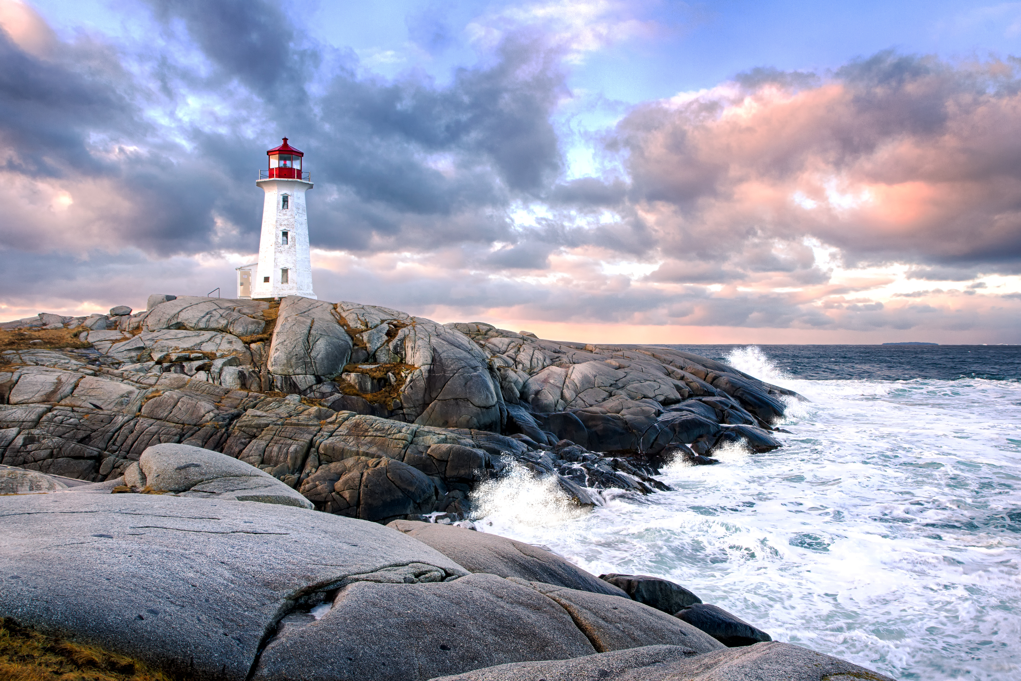 Lighthouse on rocky shore with waves crashing and cloudy sky in the background
