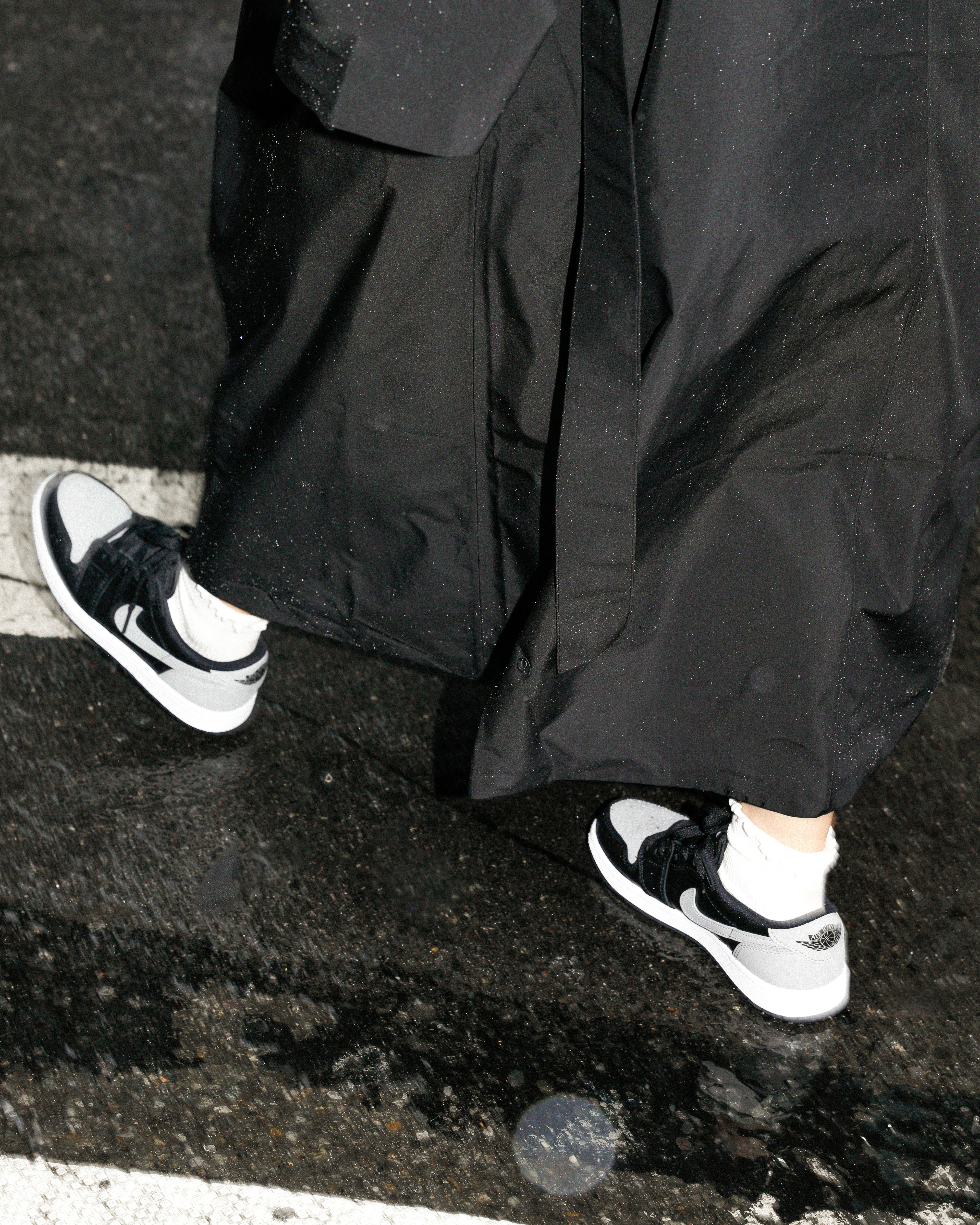 Person in black trousers and white socks wearing iconic black and white sneakers stepping onto a street