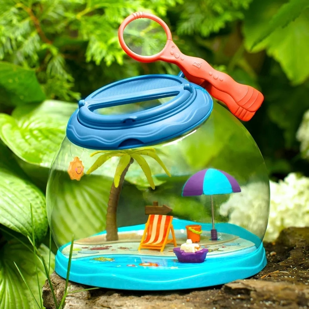 A small portable sandbox with miniature beach accessories and a magnifying glass designed for observing bugs